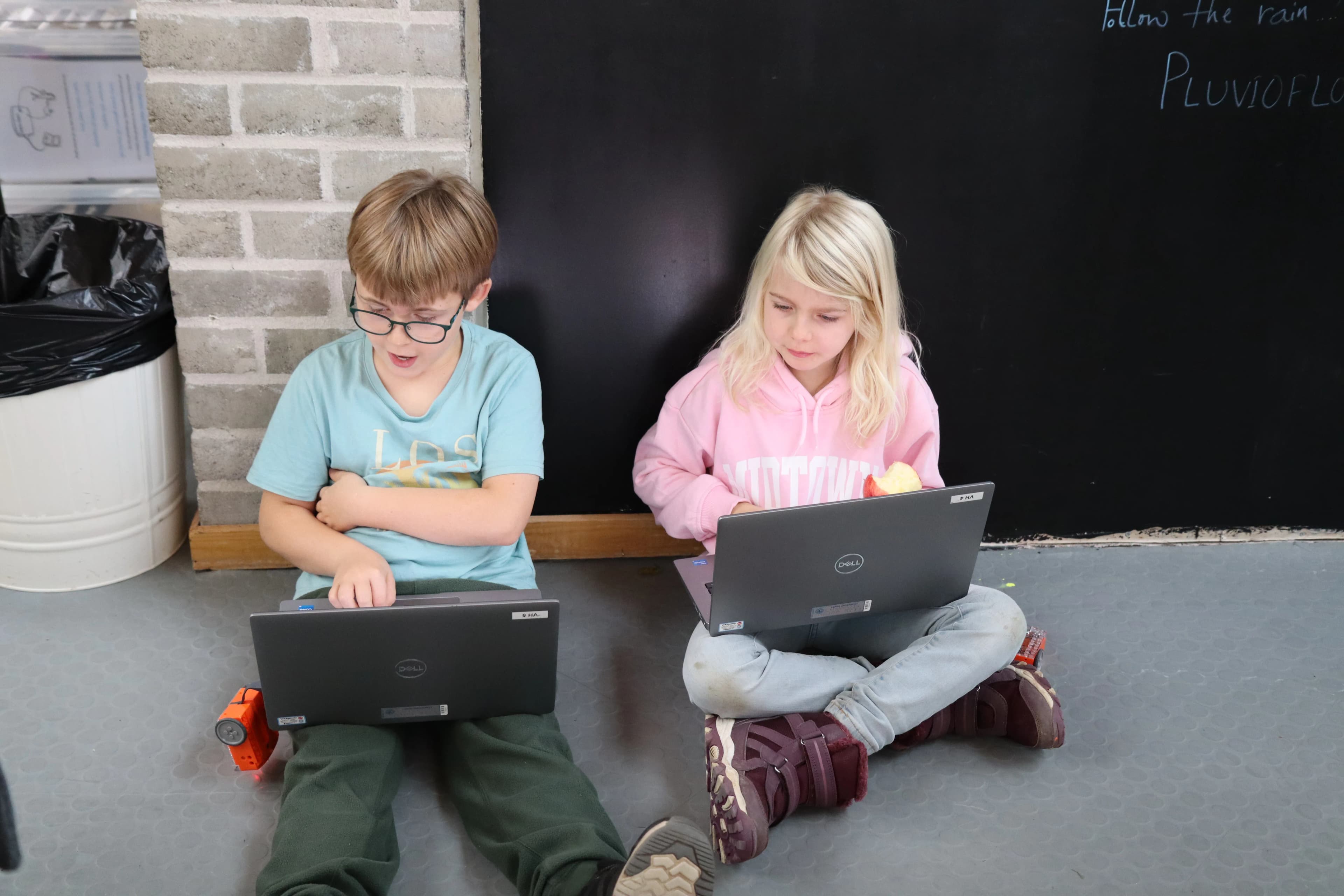 Två deltagare sitter på golvet och kodar på varsin laptop