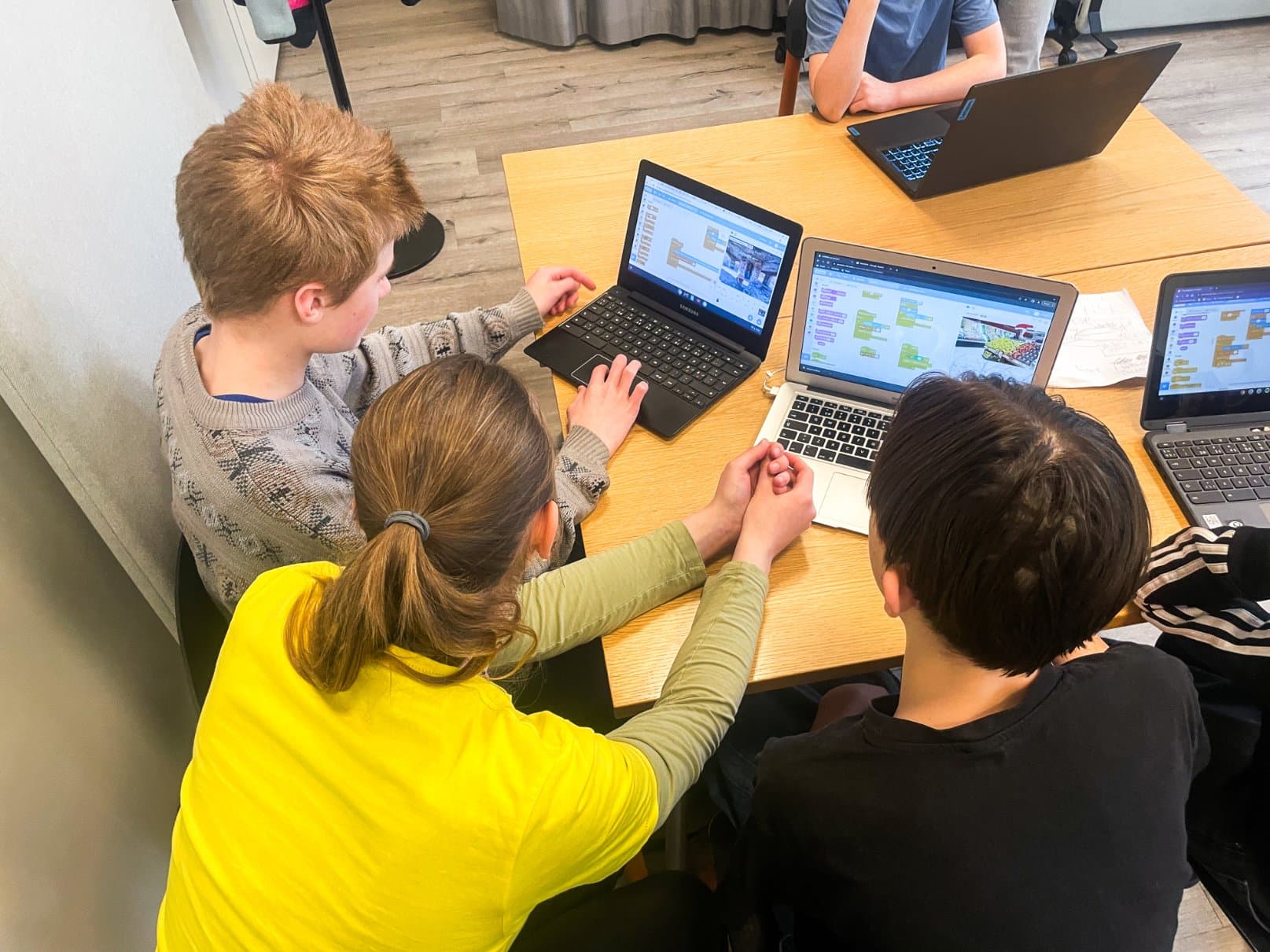 En ledare lutar sig in och hjälper två barn med ett Scratch-projekt