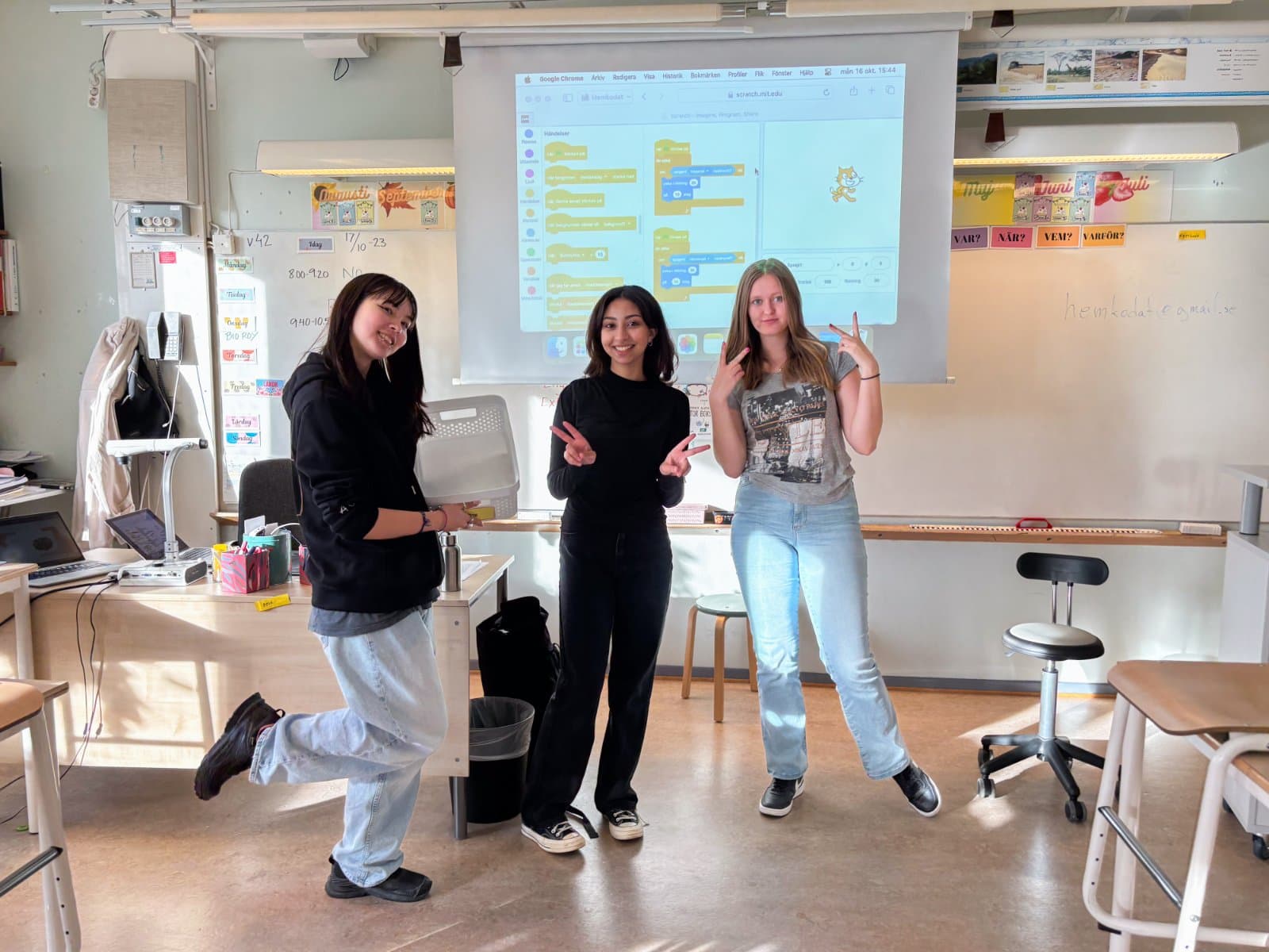 Tre unga ledare poserar framför duken med ett Scratch-projekt