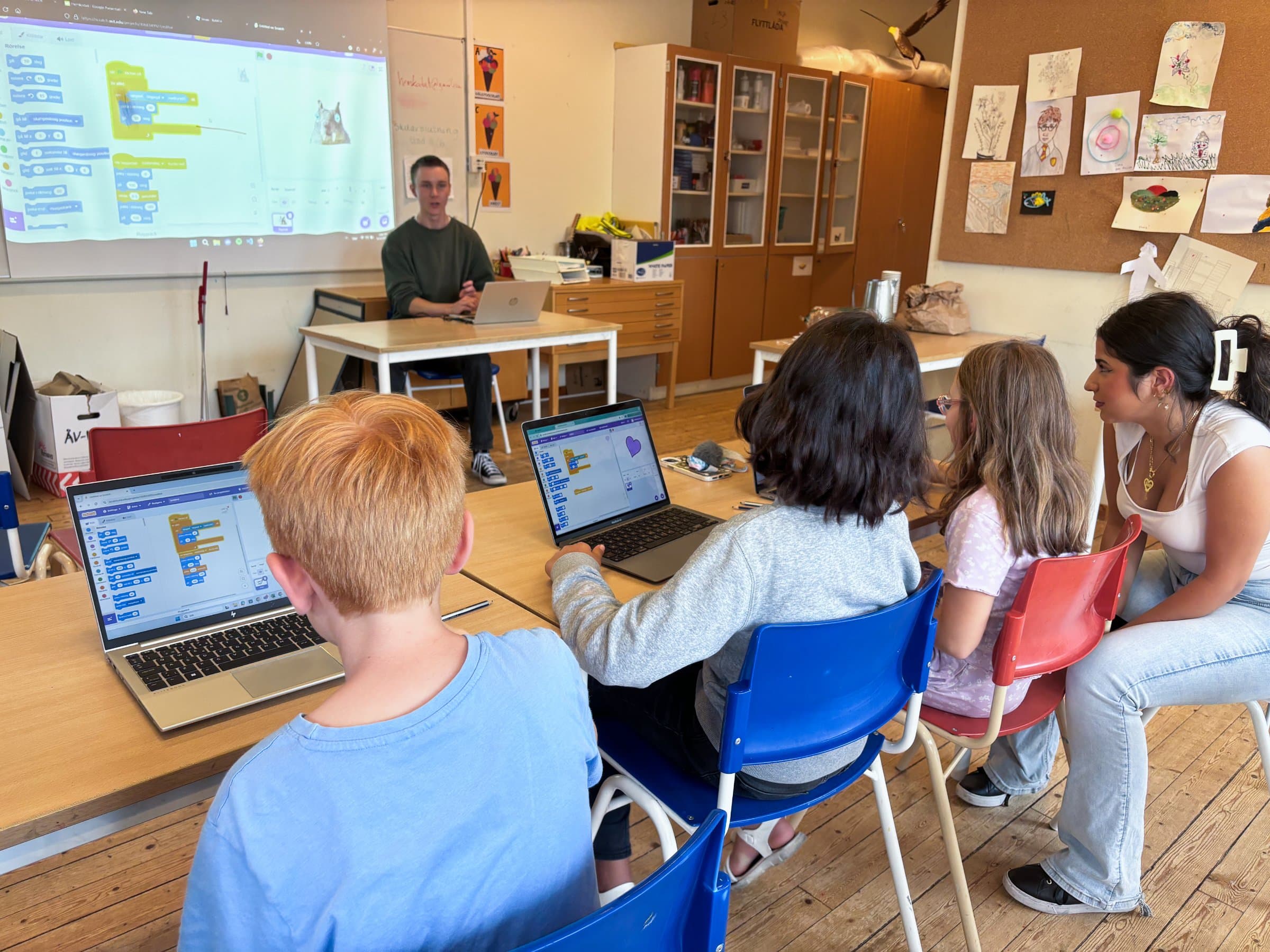 En ledare går igenom ett Scratch-projekt medan barnen arbetar vid sina datorer
