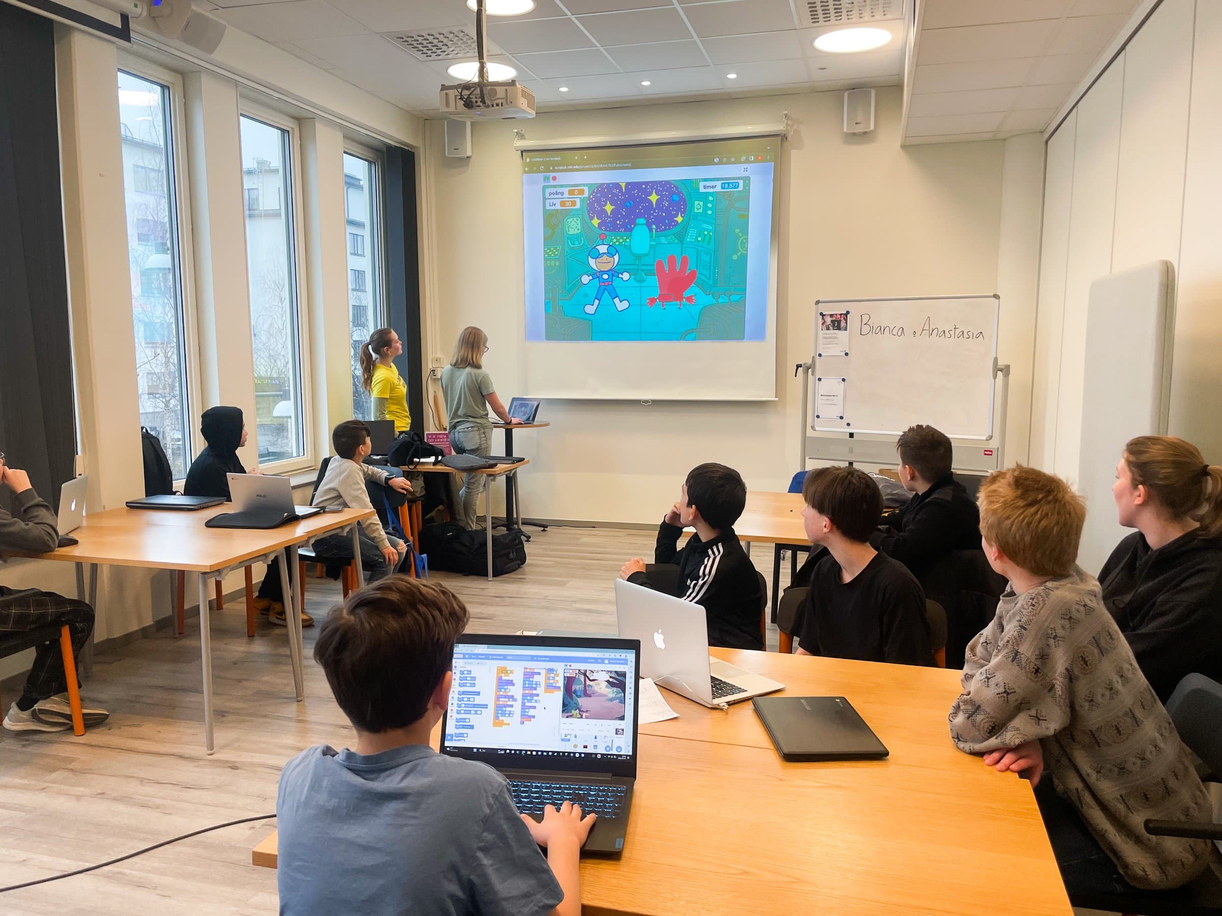 Barn följer ett egenbyggt spel på projektorduken medan två ledare visar längst fram i rummet