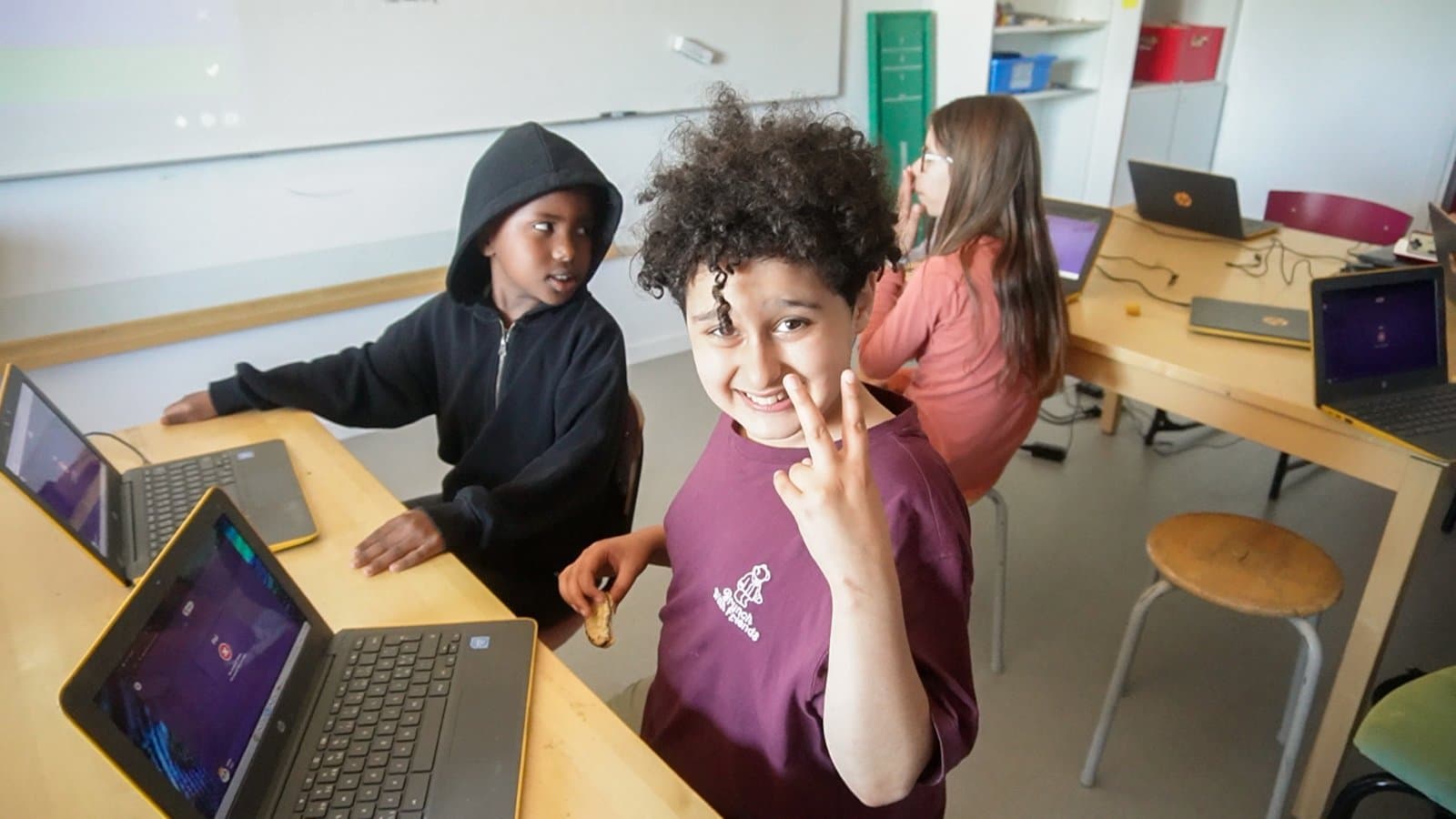 Ett barn ler och gör peacetecken vid datorerna under en teknikträff